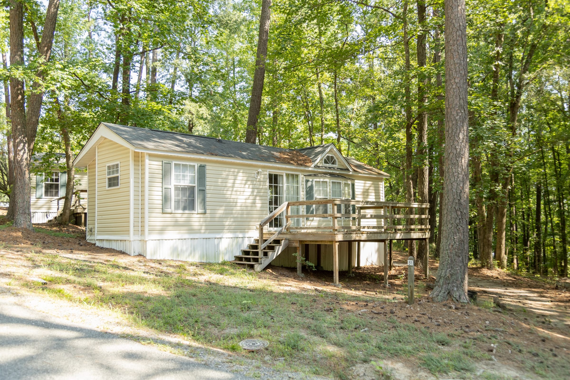 Cream rental cottage with deck and steps among hardwoods