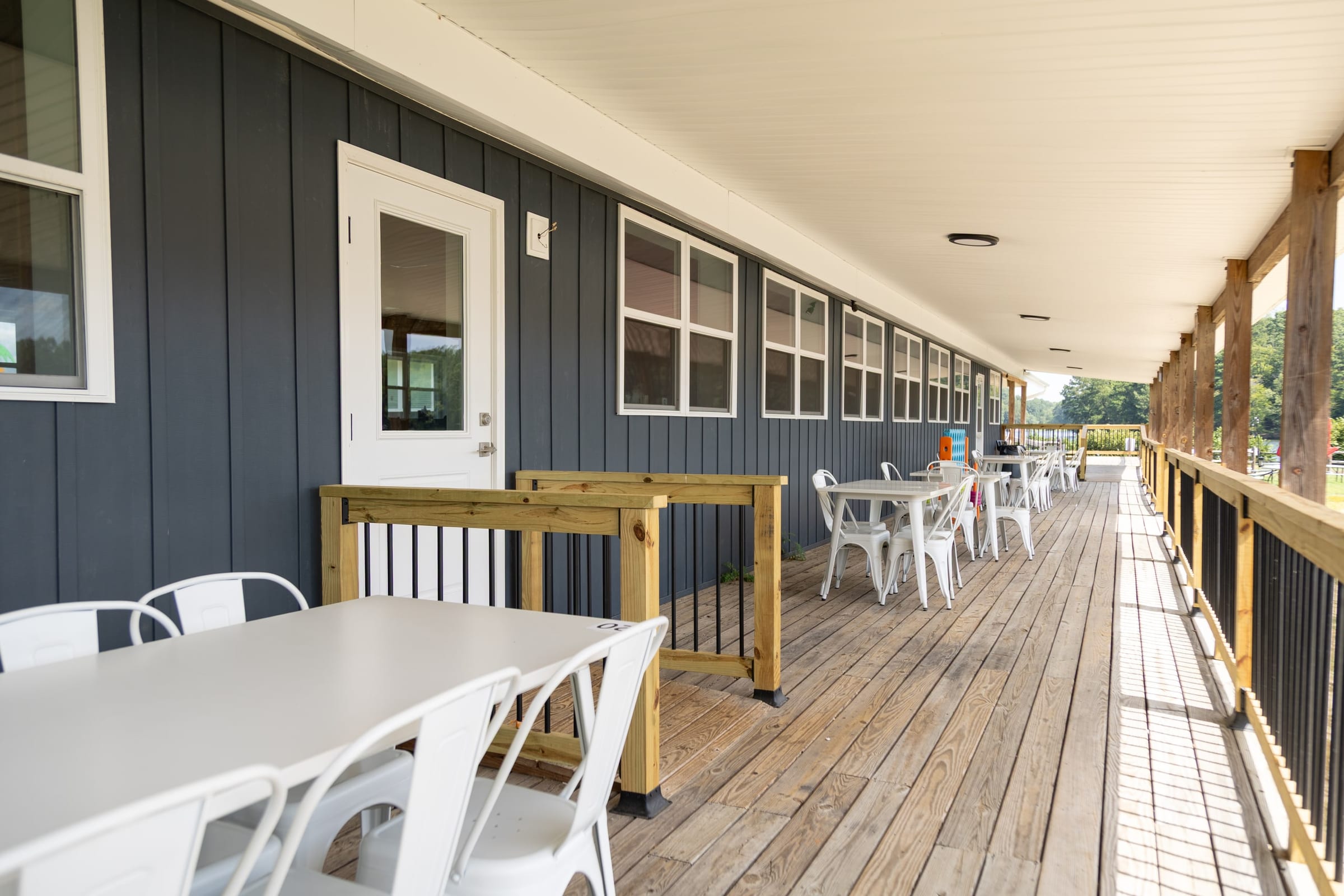 Long navy-sided porch with white metal tables down the new deck
