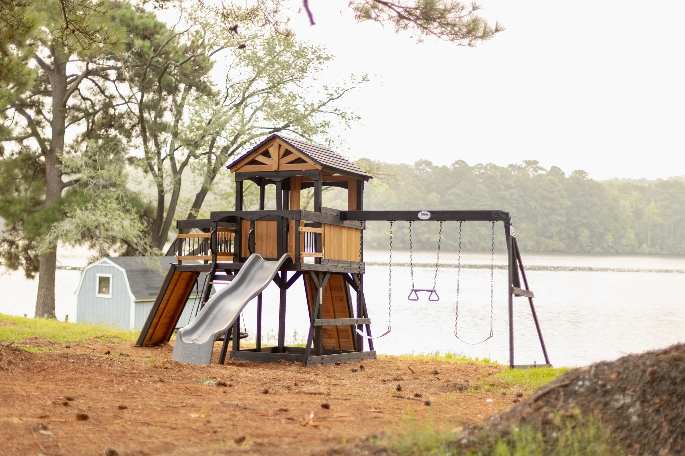 Lakeside wooden playground with a slide, climbing tower, and swings